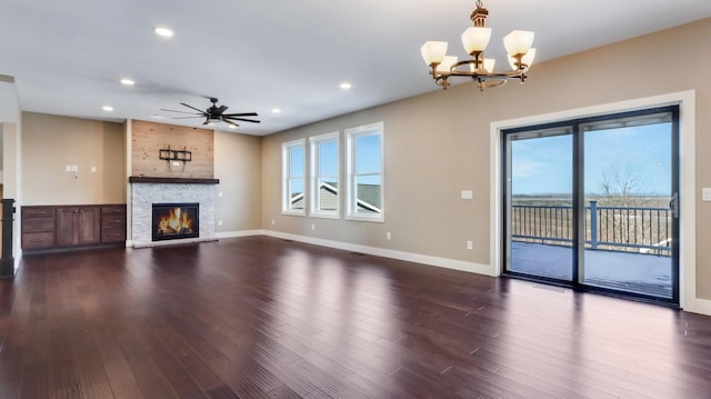 unfurnished living room featuring wood-type flooring, a stone fireplace, ceiling fan with notable chandelier, and a wealth of natural light