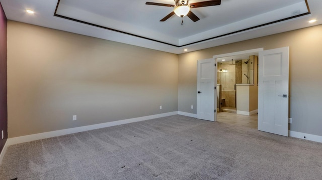 unfurnished bedroom with a raised ceiling, connected bathroom, and light carpet