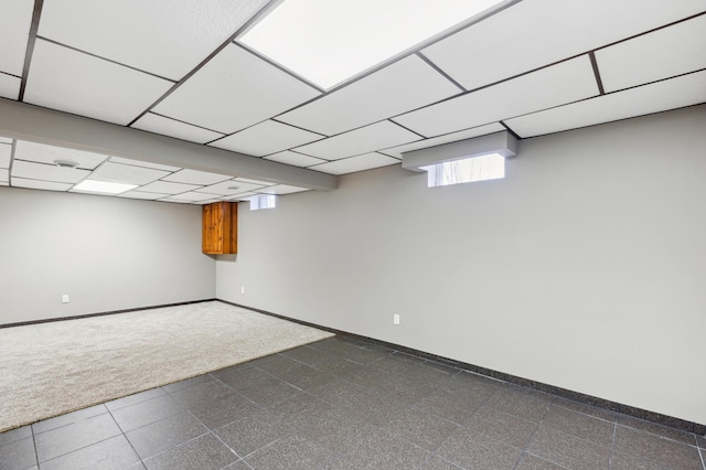 basement featuring dark colored carpet and a paneled ceiling