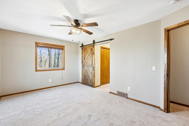 unfurnished bedroom featuring ceiling fan, a barn door, light carpet, and a textured ceiling