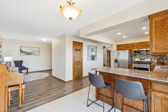 kitchen with stone counters, light tile patterned flooring, decorative backsplash, kitchen peninsula, and stainless steel appliances