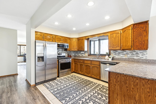 kitchen with appliances with stainless steel finishes, sink, backsplash, and light wood-type flooring