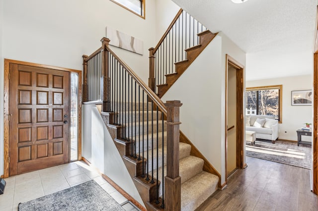 foyer entrance with a towering ceiling, a textured ceiling, and light wood-type flooring