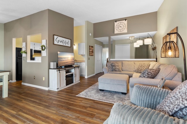 living area featuring dark wood-style floors, baseboards, and a towering ceiling