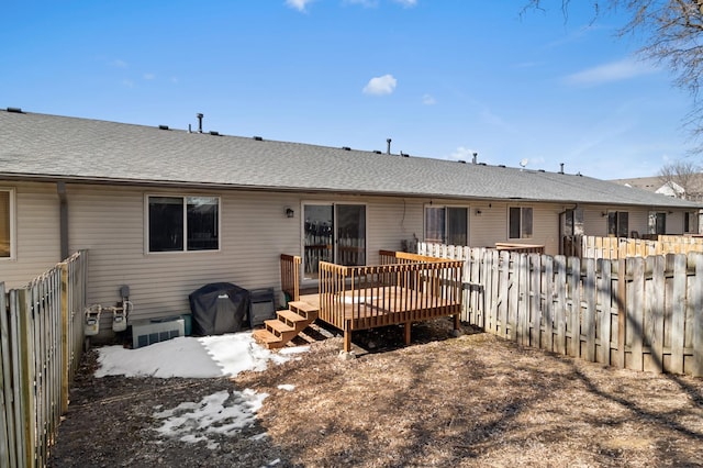 back of house with a shingled roof, a deck, and fence