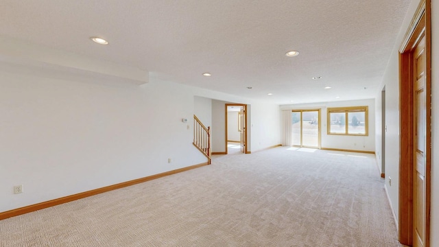 spare room featuring light carpet, stairway, and baseboards