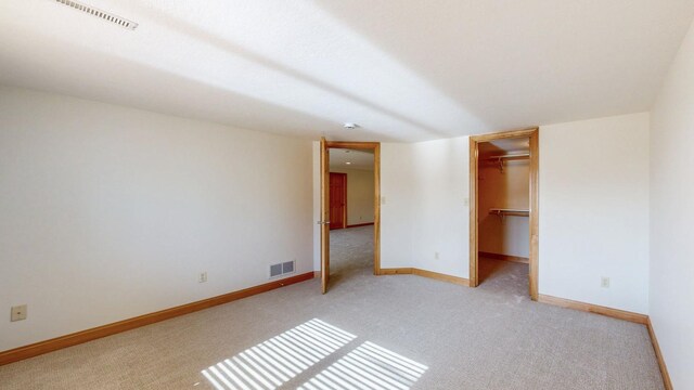 unfurnished bedroom featuring a spacious closet, baseboards, visible vents, and light carpet