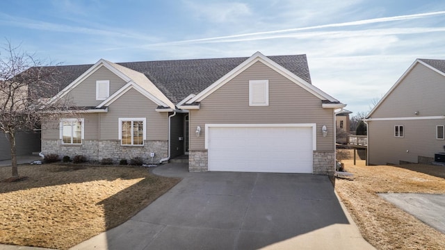 view of front of home featuring an attached garage, stone siding, driveway, and roof with shingles