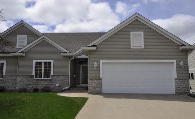 view of front facade with a shingled roof, a front yard, driveway, and stone siding