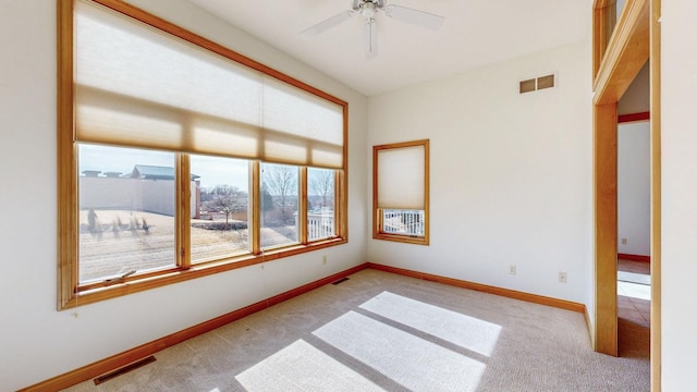 carpeted empty room with baseboards, a ceiling fan, and visible vents