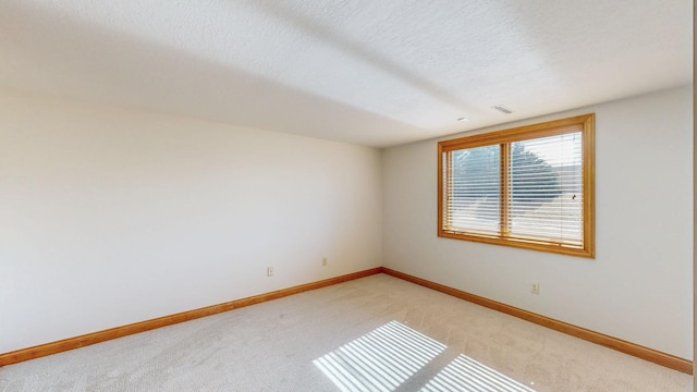 empty room with a textured ceiling, baseboards, visible vents, and light carpet