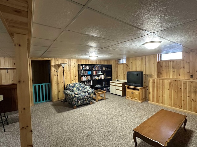 basement featuring a paneled ceiling, wood walls, and carpet