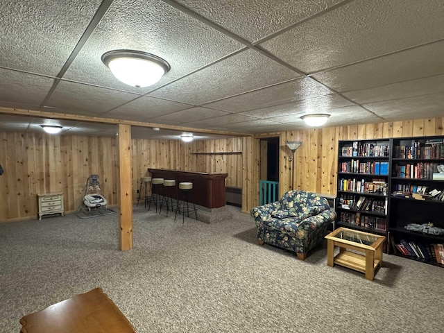 basement with carpet flooring, bar, a drop ceiling, and wooden walls