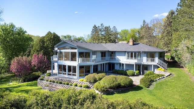 back of property featuring a balcony, a sunroom, and a yard