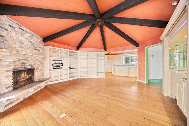 unfurnished living room with a brick fireplace, lofted ceiling with beams, and light hardwood / wood-style floors