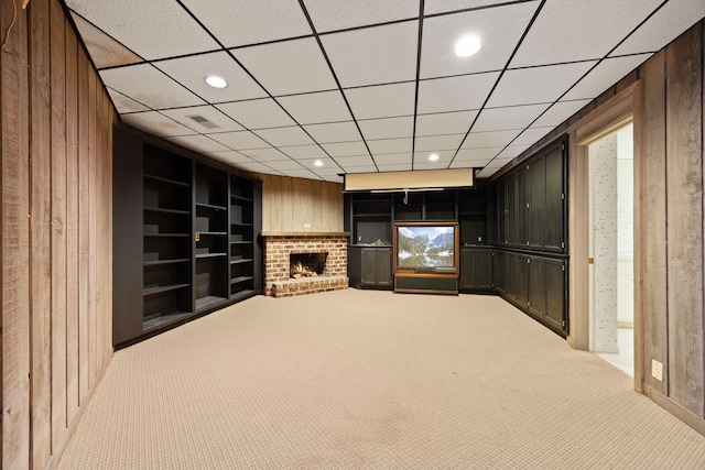 unfurnished living room with wooden walls, built in features, light colored carpet, a brick fireplace, and recessed lighting