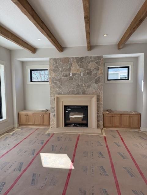 unfurnished living room with beamed ceiling, a glass covered fireplace, and baseboards