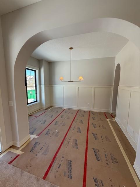 empty room featuring arched walkways, wainscoting, and a decorative wall