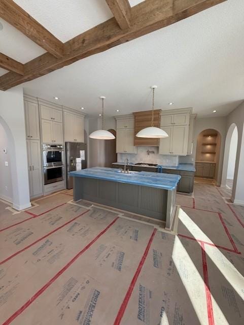 kitchen with arched walkways, a kitchen island with sink, stainless steel appliances, baseboards, and beam ceiling