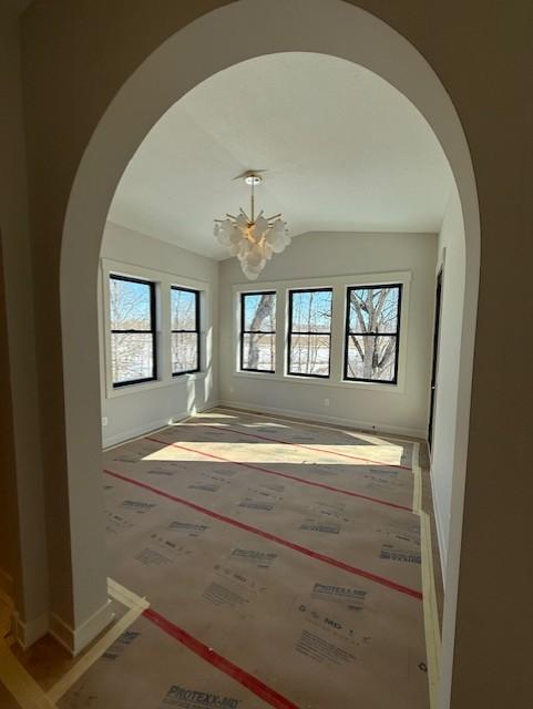 spare room featuring lofted ceiling, baseboards, arched walkways, and a notable chandelier