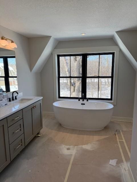 full bath with a freestanding tub, vaulted ceiling, a textured ceiling, and vanity