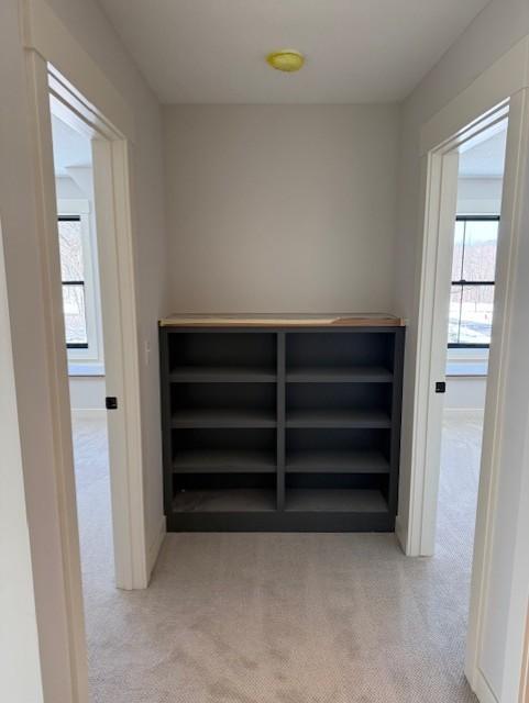 hallway with baseboards and light colored carpet