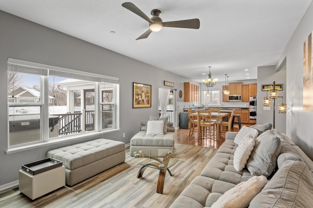 living area featuring light wood-type flooring, baseboards, and ceiling fan with notable chandelier