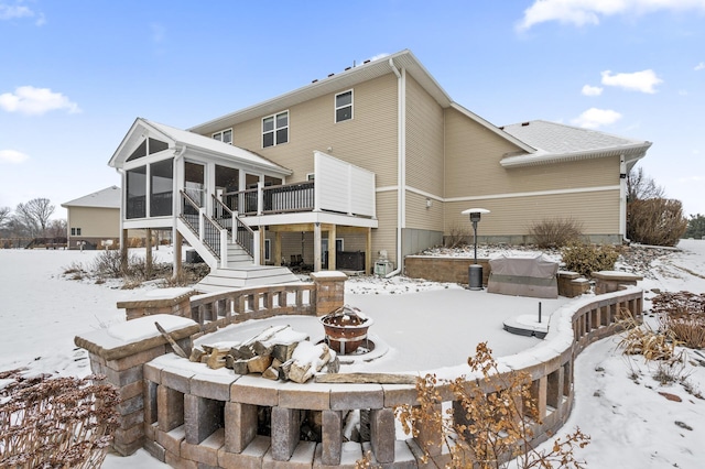 snow covered rear of property with a fire pit, a sunroom, stairway, and a wooden deck