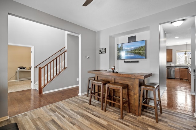 bar with a dry bar, stairway, stainless steel dishwasher, wood finished floors, and baseboards