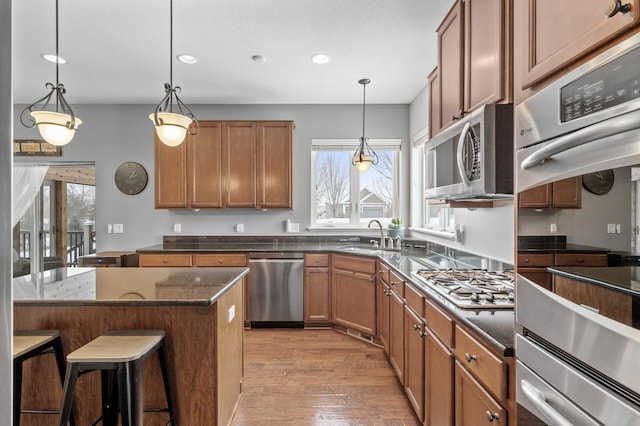 kitchen with stainless steel appliances, a kitchen breakfast bar, hanging light fixtures, light wood-type flooring, and brown cabinetry