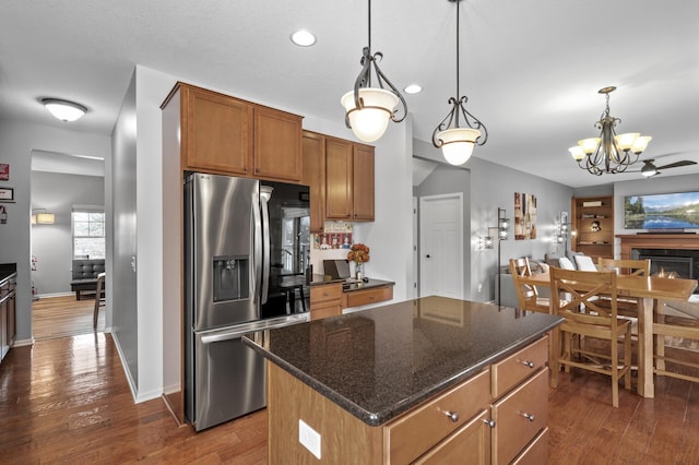 kitchen with stainless steel fridge with ice dispenser, a kitchen island, dark wood-type flooring, hanging light fixtures, and a fireplace