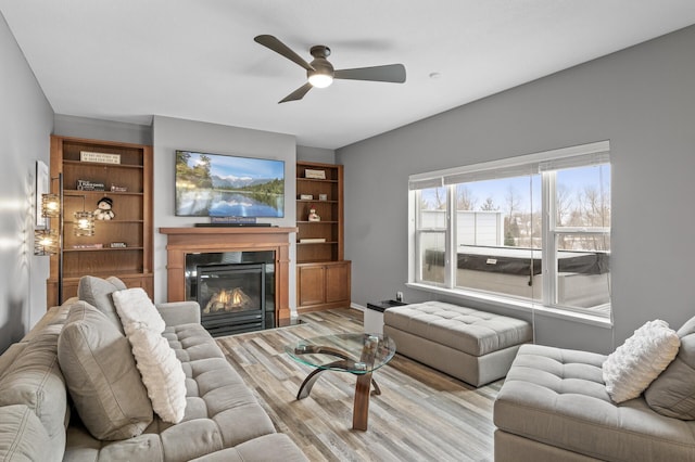 living area featuring ceiling fan, wood finished floors, and a glass covered fireplace