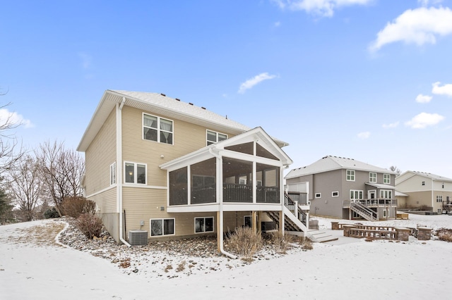 snow covered house featuring a sunroom, stairs, and central AC unit