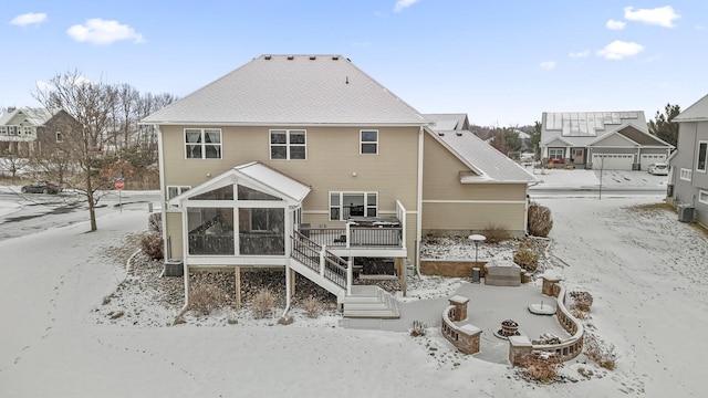 snow covered back of property featuring a shingled roof, stairway, a sunroom, central AC, and a wooden deck