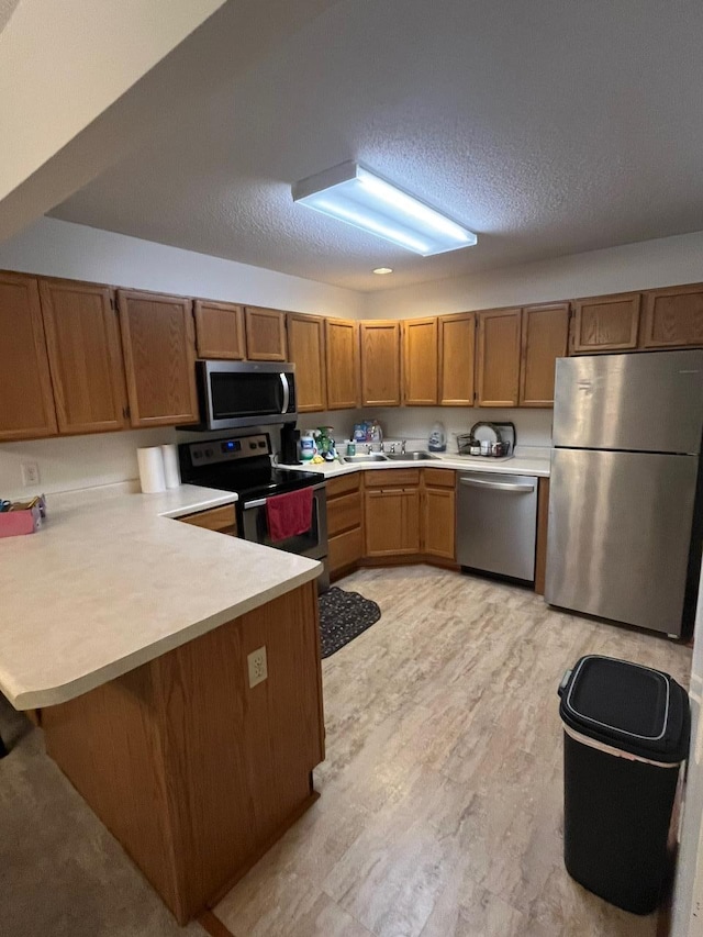 kitchen featuring sink, kitchen peninsula, a textured ceiling, and appliances with stainless steel finishes