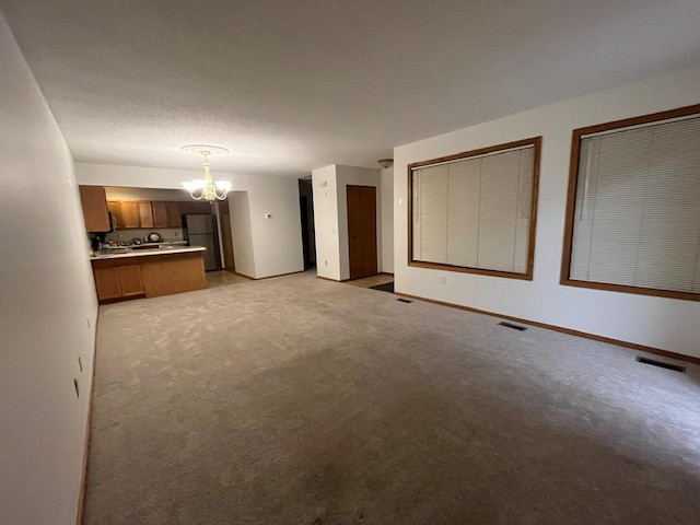 unfurnished living room featuring a textured ceiling, light carpet, and a notable chandelier