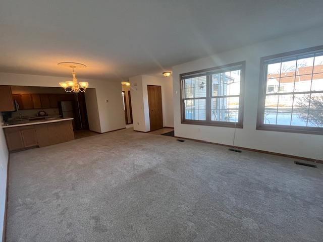 unfurnished living room featuring visible vents, light carpet, baseboards, and a chandelier