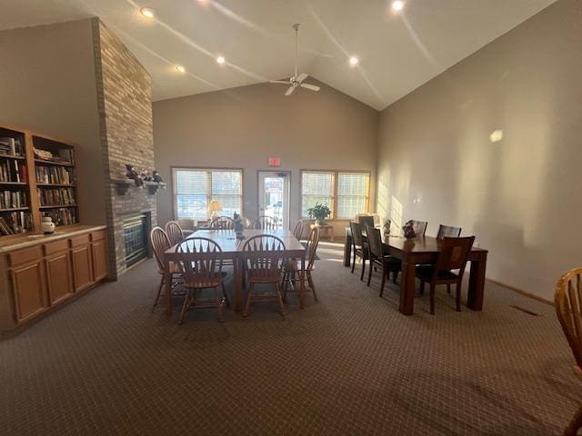 carpeted dining area with a healthy amount of sunlight, a fireplace, high vaulted ceiling, and a ceiling fan