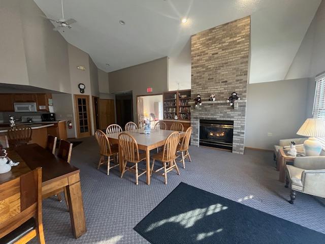 dining space with carpet flooring, high vaulted ceiling, and a large fireplace