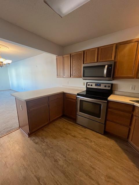 kitchen with appliances with stainless steel finishes, a peninsula, light wood finished floors, a chandelier, and light countertops