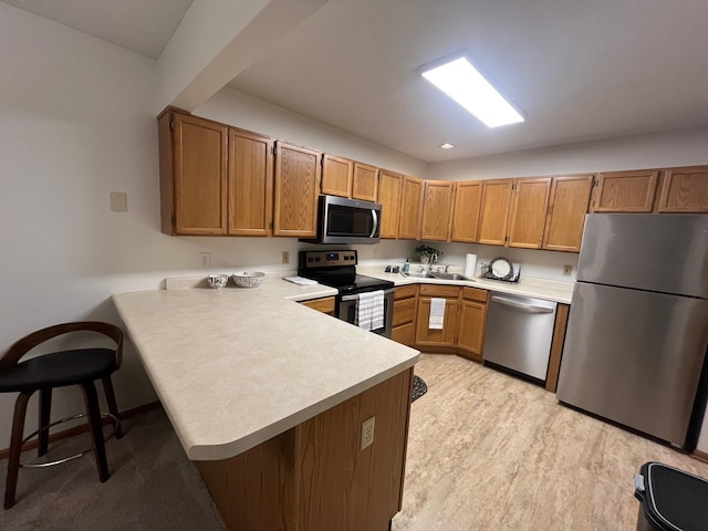 kitchen featuring light countertops, light wood-style flooring, appliances with stainless steel finishes, a peninsula, and brown cabinetry