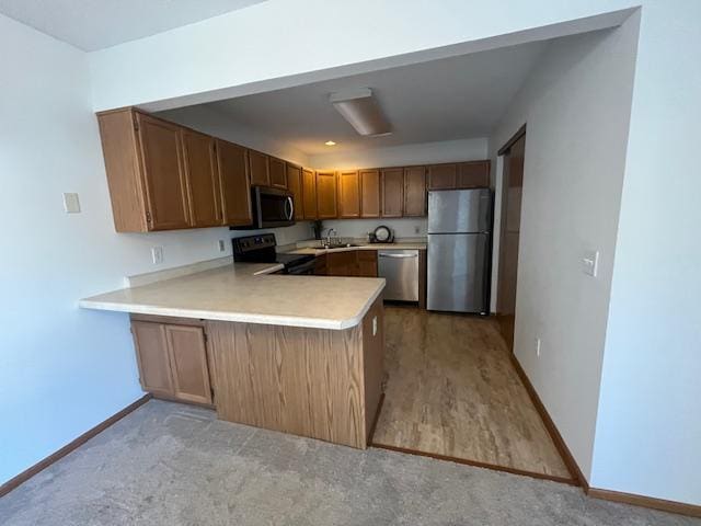 kitchen featuring a sink, stainless steel appliances, a peninsula, light countertops, and baseboards