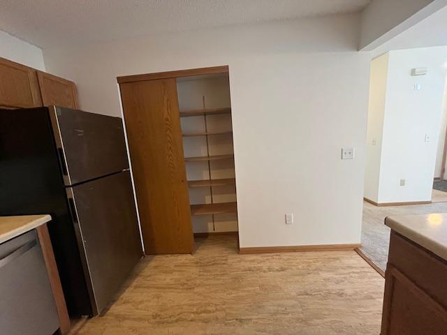 kitchen with baseboards, light wood finished floors, freestanding refrigerator, light countertops, and dishwasher