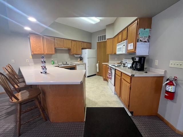 kitchen featuring a kitchen bar, visible vents, white appliances, a peninsula, and light countertops