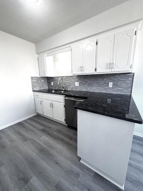 kitchen with sink, white cabinetry, dark hardwood / wood-style floors, stainless steel dishwasher, and kitchen peninsula