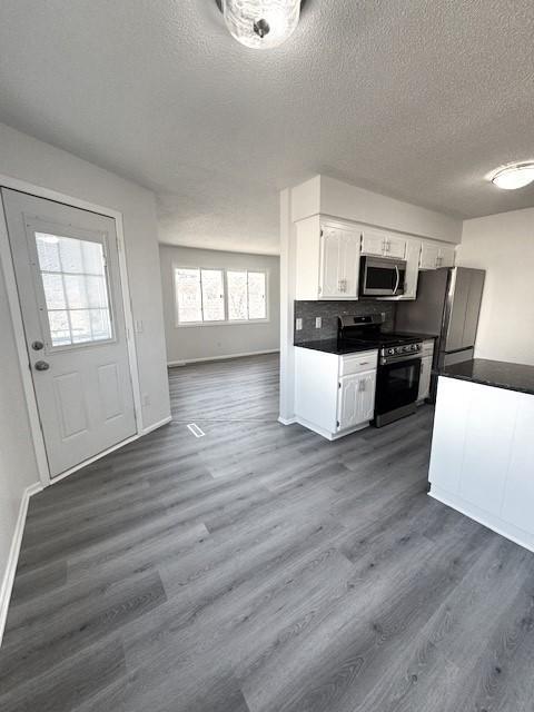 kitchen with stainless steel appliances, white cabinetry, dark wood-type flooring, and decorative backsplash