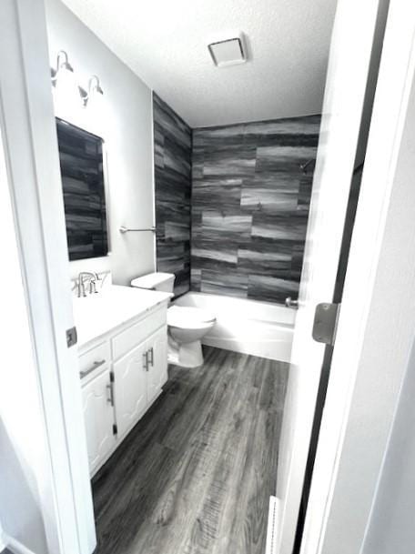 full bathroom with hardwood / wood-style floors, tiled shower / bath combo, vanity, toilet, and a textured ceiling