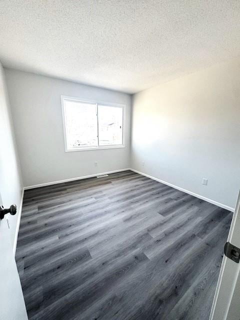 spare room featuring dark wood-type flooring and a textured ceiling