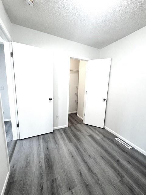 unfurnished bedroom with a walk in closet, dark hardwood / wood-style flooring, a closet, and a textured ceiling