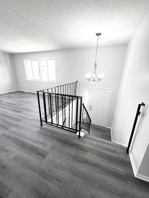 staircase featuring an inviting chandelier, wood-type flooring, and a textured ceiling